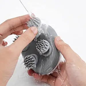 Gray silicone cleaning brush with bristles held by hands against a white background